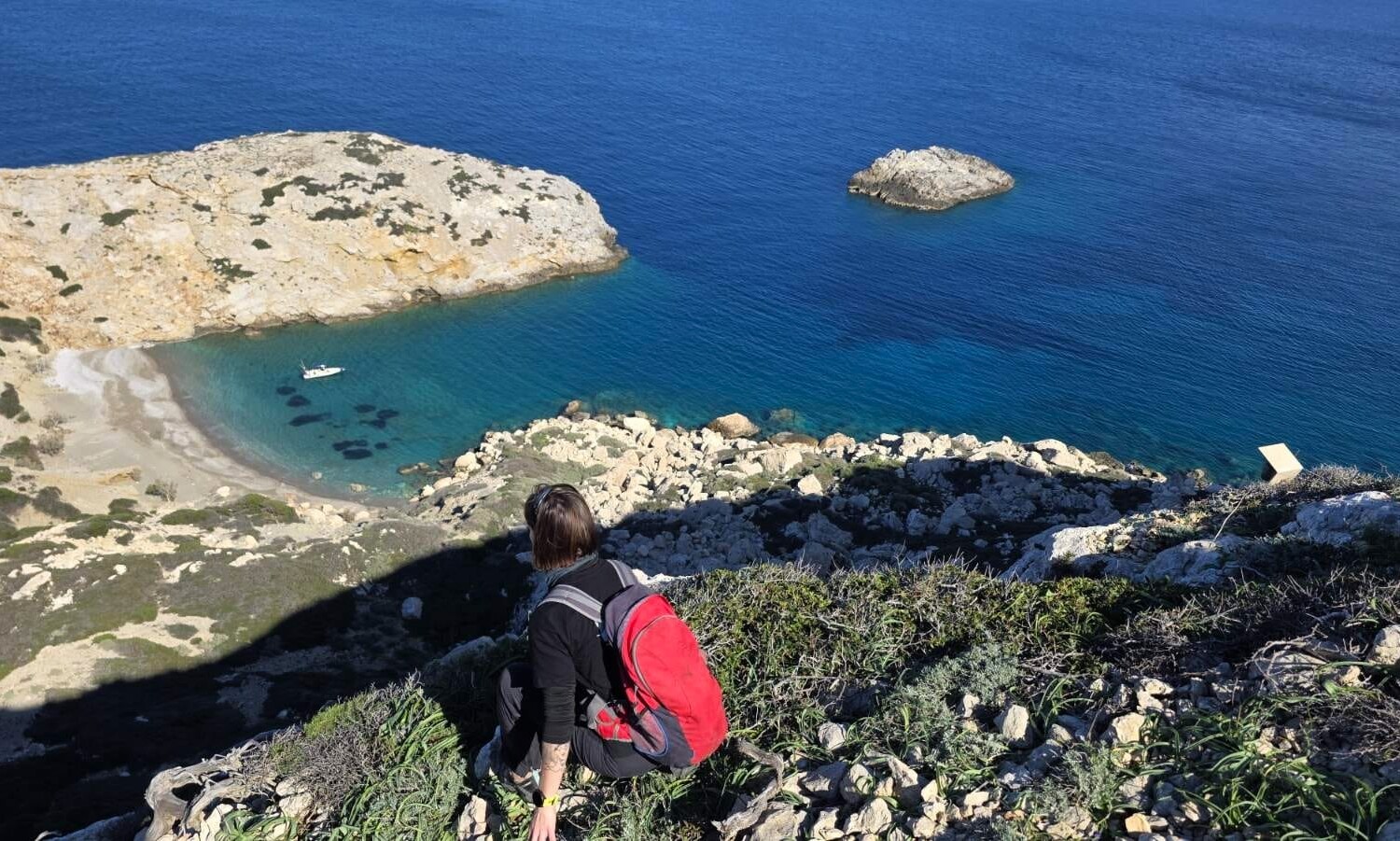 Κοιτάζοντας από την κορυφή βορειοανατολικά μπρος το λιμανάκι στο ανατολικό πλευρό του νησιού, όπου είναι αγκυροβολημένο το φουσκωτό της NCC. Μπροστά μας βρίσκεται το γκρεμνό 50 μέτρων.